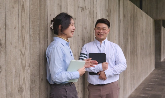 Two business people smiling and standing against a wall